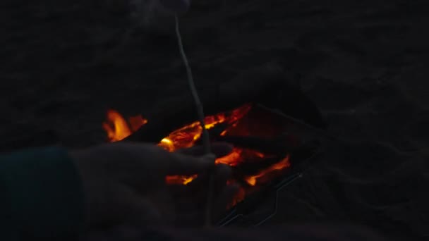 那位年轻女子正在海滩上的火堆上煎棉花糖 太阳已经落在了山后的红天里 — 图库视频影像