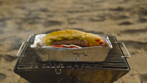 알루미늄 플레이트의 햄버거가 그릴에 가열되고 있습니다 해변에서 피크닉 슬로우 — 비디오