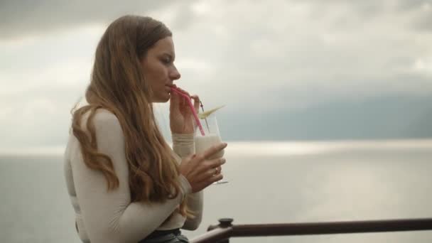 这个年轻的女人喝着鸡尾酒 欣赏高山上的大海 在海上一家餐馆里约会 — 图库视频影像