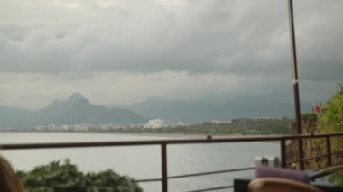 Denizdeki bir uçurumun kenarındaki bir restoranda genç bir kadın, düşünceli bir şekilde bakıyor ve elinde bir peçeteyle oyalanıyor. Şehir geride kaldı.