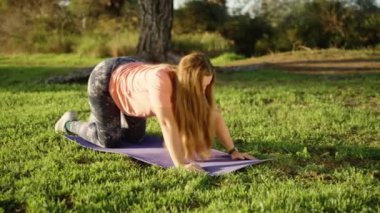 Yoga dersleri şafakta ormanda. Yeşil çimlerin üzerinde köpek pozisyonunda genç bir kadın..