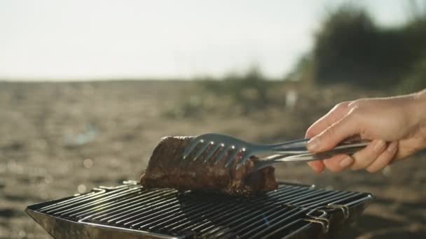 海でビーチでピクニックし 炭のステーキを揚げる 舌で一つずつ曲げる — ストック動画