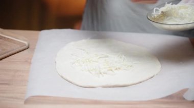 Genç bir kadın pizza hamuruna rendelenmiş peynir koyar.
