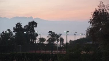 Gün batımı, güneş dağların ardında battı. İnsanlar büyük tenis oynuyorlar. Denizde ve hurma ağaçlarında..