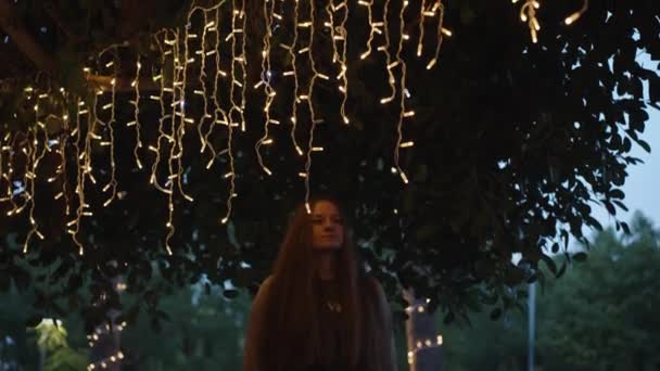 Wieczorne Oświetlenie Drzewa Wiszące Girlandy Przemijająca Dziewczyna Dotyka Jej Dłoni — Wideo stockowe