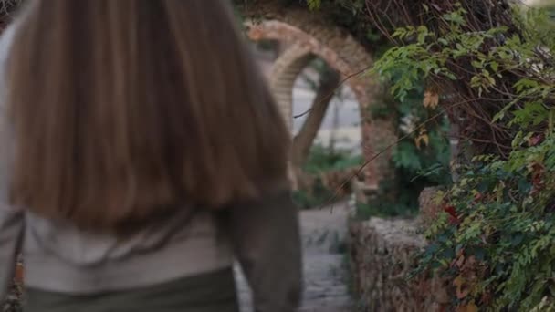 一位年轻女子走进公园 穿过石柱和灌木丛 — 图库视频影像