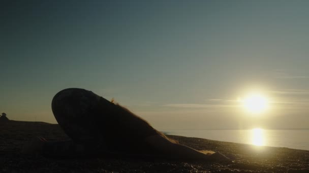 若い女性のシルエットは 海で夜明けに敷物の上に伸びています 太陽が低い — ストック動画