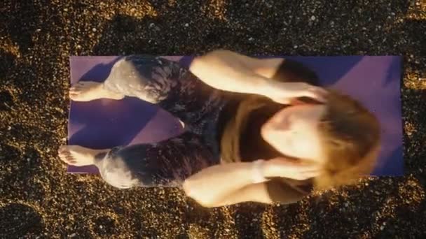 这个年轻的女人正在海边岩石沙滩上的垫子上健身 顶视图 — 图库视频影像