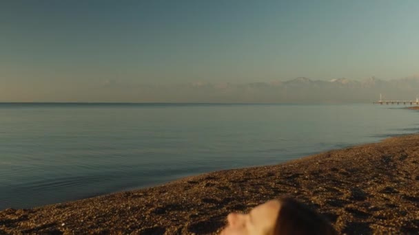 朝早く 若い女性は海岸でのフィットネス後に休んでいる 山からのカメラの焦点は少女に行く — ストック動画