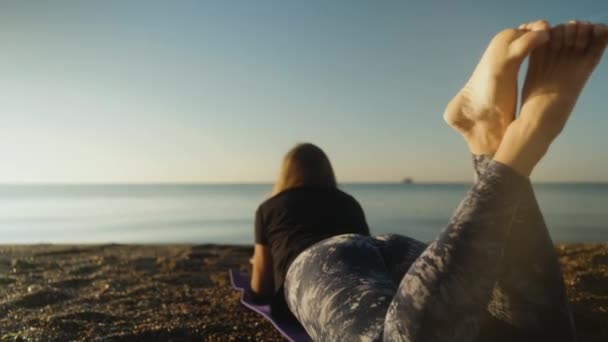 清晨的大海里 一个穿着紧身裤的年轻女子躺在一块地毯上 看着石头 后视镜 — 图库视频影像