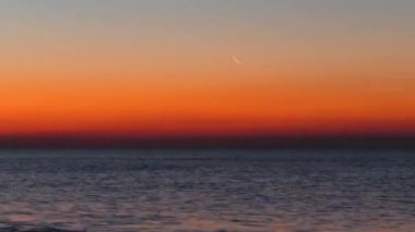 Denizin üstünde Kızıl Şafak, güçlükle farkedilebilen Ay. Güneş, suyun içinden belirir. Zaman Uygulaması