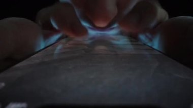 Karanlıktaki bir adam hızlı bir şekilde akıllı telefonuyla internetten video izliyor. Dolly Kaypak çok yakın çekim. İnternetteki yaşam kavramı