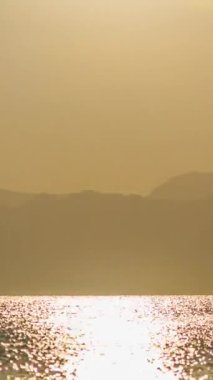 Zaman aşımı, Denizde Altın Gün Batımı. Güneş dağların ardında batıyor, kamera onu takip ediyor, Panorama. Sosyal ağlar için dikey.