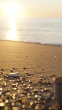 Denizde gün doğumu. Soğuk bir sabah, elinde sıcak içecek olan bir kupa kumsalda duruyor ve ondan buhar çıkıyor. Yakın plan. Dikey video Sosyal Ortamı