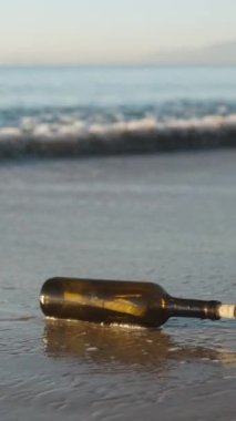 Bir cam şişe ve bir mektup, bir dalga onu kıyıya fırlatıyor, ağır çekim. Dikey video Sosyal Ortamı