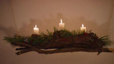 Yılbaşı süslemeleri ve mumlar, ağaç kabuğundan yapılmış bir dal parçasına asılır. Mumların gölgesi beyaz duvara düşüyor..