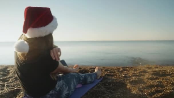 Een Jonge Vrouw Met Een Rode Kerstmuts Zit Het Zandstrand — Stockvideo