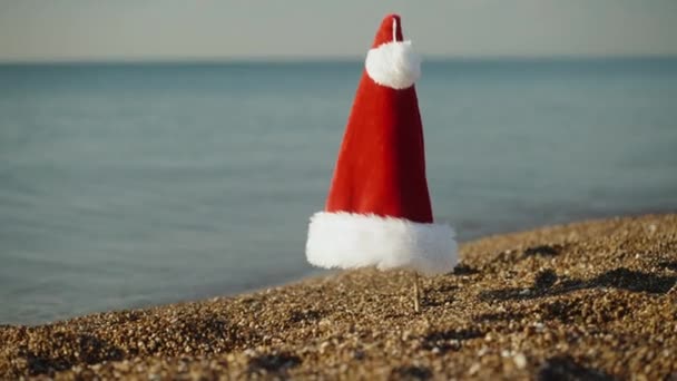赤いサンタは早朝の日の出に海でビーチで帽子をかける — ストック動画