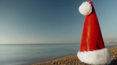 Kırmızı Noel Baba şapkası kumlu sahilde güneşli bir sabahın erken saatlerinde, yakın planda tutulur..
