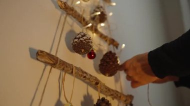 Genç bir kadın duvara Noel süsü, fenerler ve dallarla süslenmiş süsler asıyor..