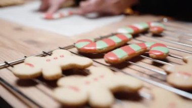 Küçük bir torbadan beyaz krema kullanan kadın, zencefilli kurabiyeyi baston şekeri şeklinde kaplıyor..