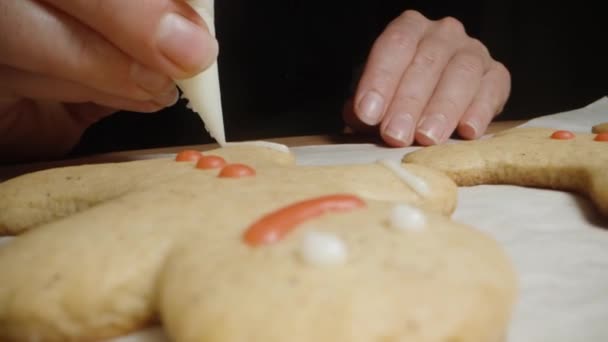 这个女人从一个糕点袋中挤出一条细细的白糖水在姜饼上 饼干的形状像个小人物 特写镜头 — 图库视频影像
