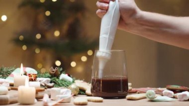 Evde Noel içeceği, masada tatlılar, ve bir kadın hamur torbasından kakaoya krema sıkıyor..