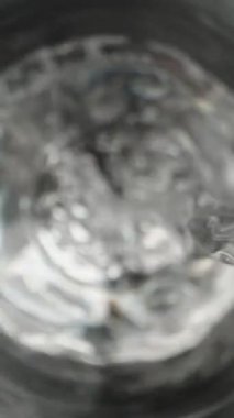 Cam şişeden temiz su döküyorum, kamera bardağın içinde, üst tarafta. Kaypak Dolly çok yakın çekim yapıyor. Laowa Sondası Dikey Video.