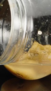 Bir cam şişenin makro videosu, kayısıdan meyve suyu. Dolly kayısı şişesinin içinde, yakın plan, dönüşümlü. Laowa Sondası Dikey Video.