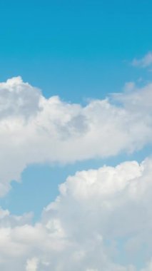 Mavi gökyüzünde her yöne doğru süzülen beyaz bulutlar. Dikey, Sosyal Ortam.