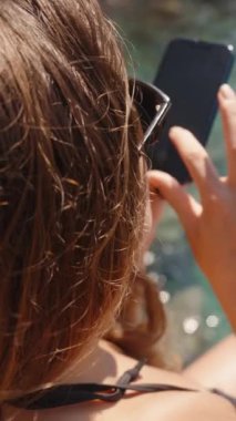 Denizde genç bir kadın, arka plandaki suya karşı bacaklarının resimlerini çekiyor. Dikey, Sosyal Ortam.