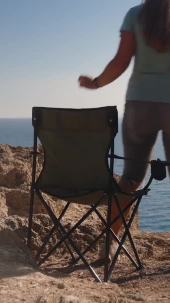 若い女性が海の崖の端に折りたたみ椅子に座っています ソーシャルメディア — ストック動画