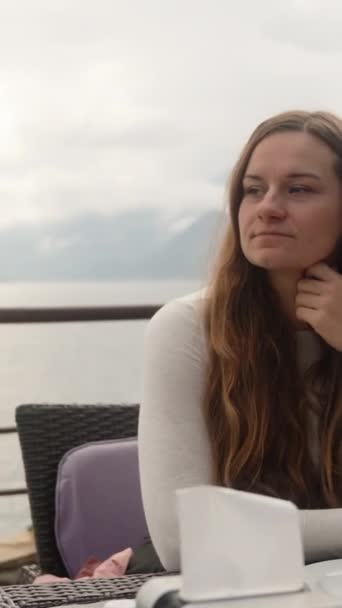 一个年轻的女人在海边悬崖上的咖啡店里 她向大海望去 垂直视频社交媒体 — 图库视频影像