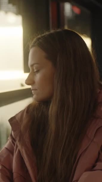 日没を見下ろすカフェのピンクのレインコートに長髪の若い女性 垂直ビデオ ソーシャルメディア — ストック動画