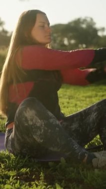 Şafakta genç bir kadın çimenlikteki ormanda spor yapıyor. Güneş ışınları saçlarına düşer. Dikey video Sosyal Ortamı.