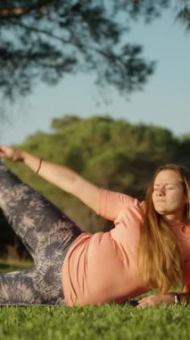 Genç kadın şafak vakti ormanda bir spor minderinde spor yapıyor. Çam ağaçları ve mavi gökyüzü. Dikey video Sosyal Ortamı.