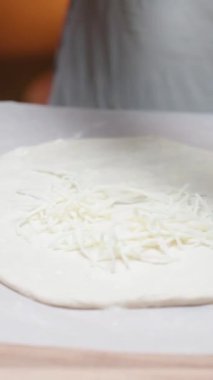 Genç bir kadın pizza hamuruna rendelenmiş peynir koyar. Dikey video Sosyal Ortamı.