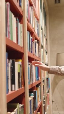Kitapçıda uzun saçlı genç bir kadın bir kitap çıkardı ve göz gezdirdi. Dikey video Sosyal Ortamı.