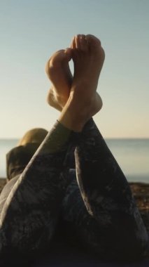 Dar taytlı genç bir kadın sahilde yatıyor, bacakları kalkıyor, bacaklarını açıyor ve kamera yavaşça içinden geçiyor ve vücudunun üzerinden kayıyor. Dikey video Sosyal Ortamı.
