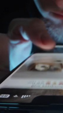 Sakallı bir adam hızla internetteki fotoğraflara bakar. Karanlıkta yaklaş, Mavi Işık. Dikey video Sosyal Ortamı.