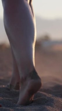 Genç kadının bacakları kumu dağıtıyor, yakın plan. Kamera onu takip ediyor. Gün batımında deniz ve sahil. Dikey, Sosyal Ortam
