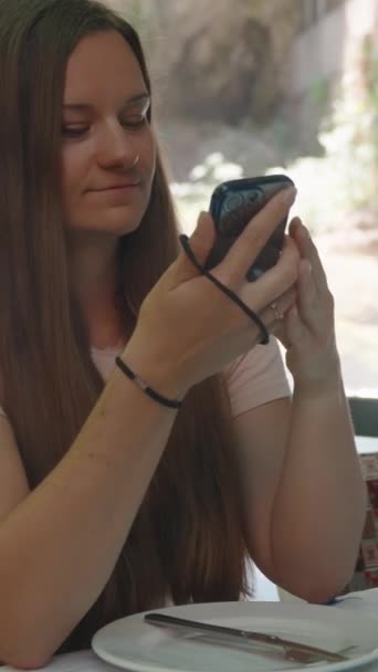这个年轻的女人自私自利 她看着手机里的照片 后面是一个瀑布 社交媒体 — 图库视频影像