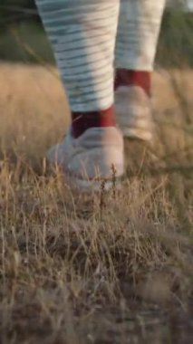 Genç kadın gün batımında kuru çimlerin üzerinde yürüyor, kamera onu aşağıdan takip ediyor, yakın plan. Dikey, Sosyal Ortam