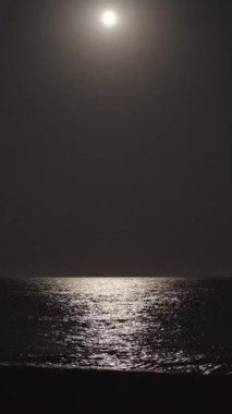 Çerçevenin ortasında büyük bir ay, okyanusu aydınlatır. Sahilde dalgalar. Dikey, Sosyal Ortam