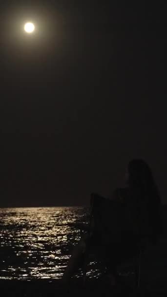 这个年轻的女人坐在海边的椅子上 望着月亮 男人走近她 — 图库视频影像