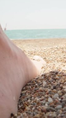 Kadınların ayakları küçük deniz taşlarına basar, yakın plan. Arka plandaki deniz. Dikey. Sosyal Medya