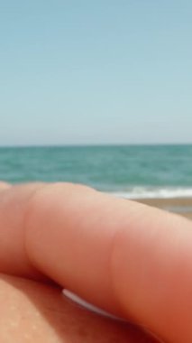 Genç kadın yanan omzunu denizin arka planına güneş kremiyle sürüyor. Kum. Büyük dalgalar. Dolly kaydırıcı. Dikey. Sosyal Medya