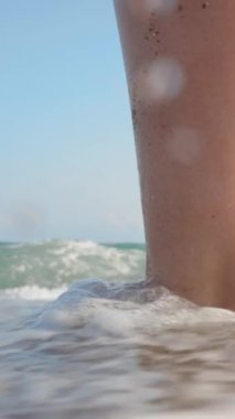 Ayaklar sahilde, yakın plan. Dalga bacaklara vurur ve kamera suyun altına girer. Dikey. Sosyal Medya