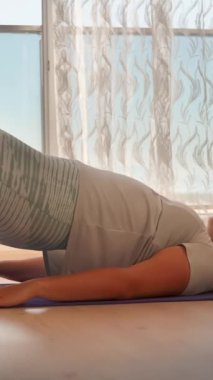 Şişman genç bir kadın mor bir paspasın üzerinde spor yapıyor. Arkadaki kalça köprüsü. Dikey. Sosyal Medya