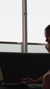 Genç kadın bir dizüstü bilgisayarda çalışıyor. Mesafeli iş. Kanepede oturuyordum. Tam bir duvar penceresi. Dikey. Sosyal Medya